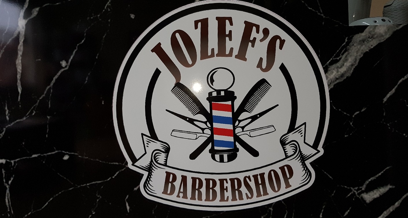 Het ronde logo van Jozef's Barbershop met een kapperspaal, scharen, kammen en een lint, op zwart marmer