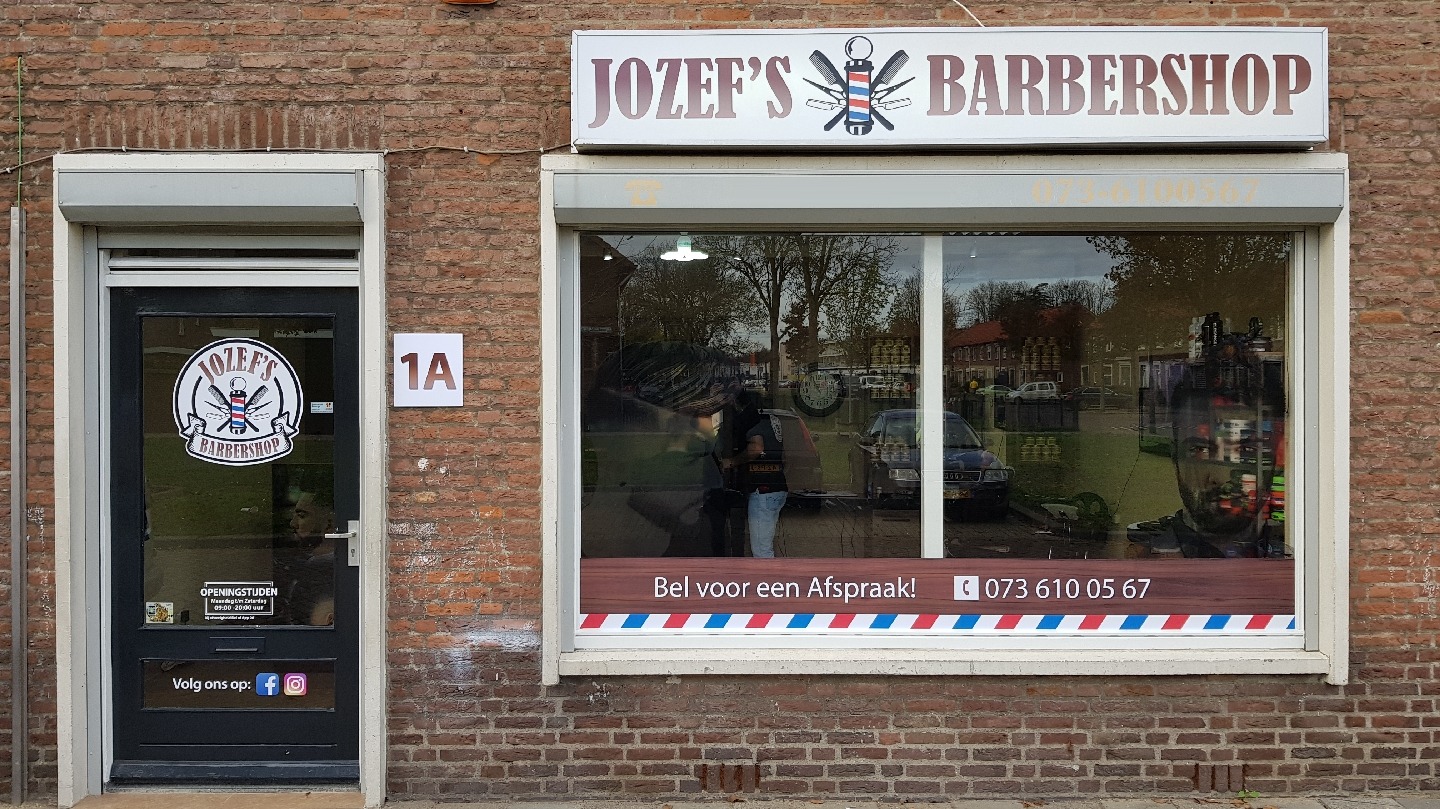 De gevel van Jozef's Barbershop aan de Pastoor Mutsaersstraat 1-A: rode baksteen, het witte uithangbord, de deur met het ronde logo en het raam met 'Bel voor een Afspraak!'