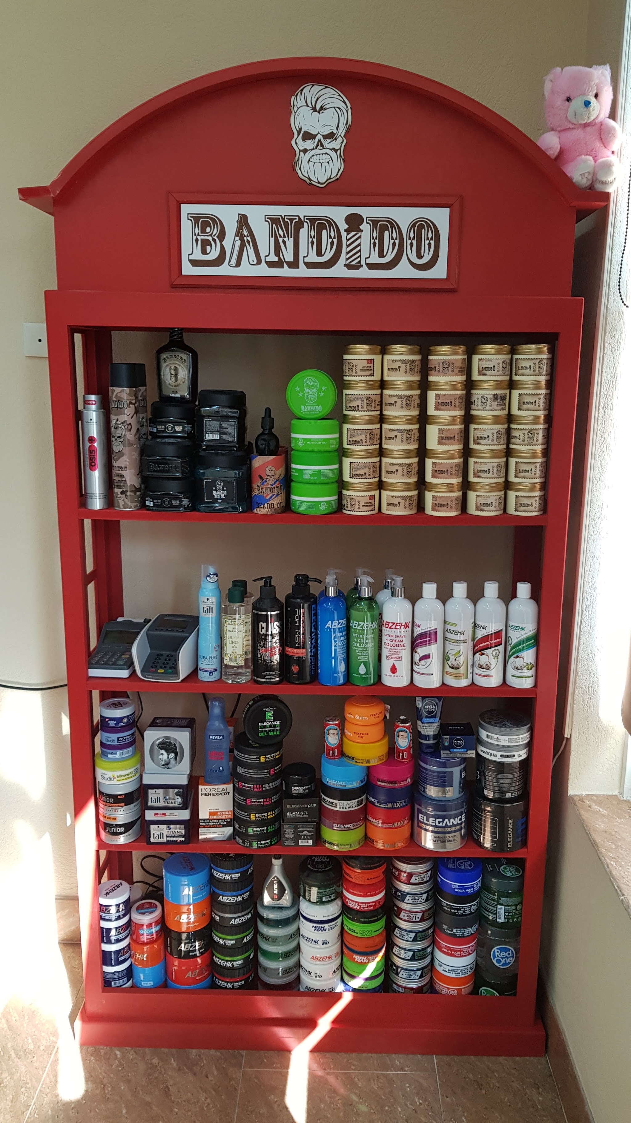 De rode Bandido-kast met een koepel en een schedel-logo bovenop, de planken vol potten, flessen en tubes